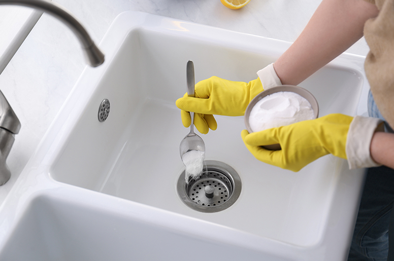 A homeowner pours baking soda into a kitchen drain 