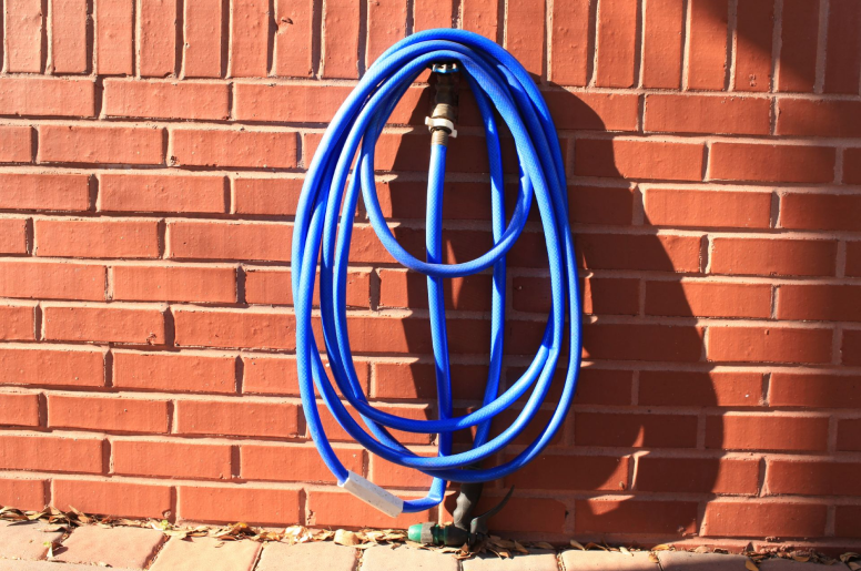 A blue garden hose hanging on a hose bib installed on a brick wall 
