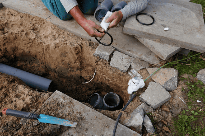 a plumber repairing a backwater valve outside of a home
