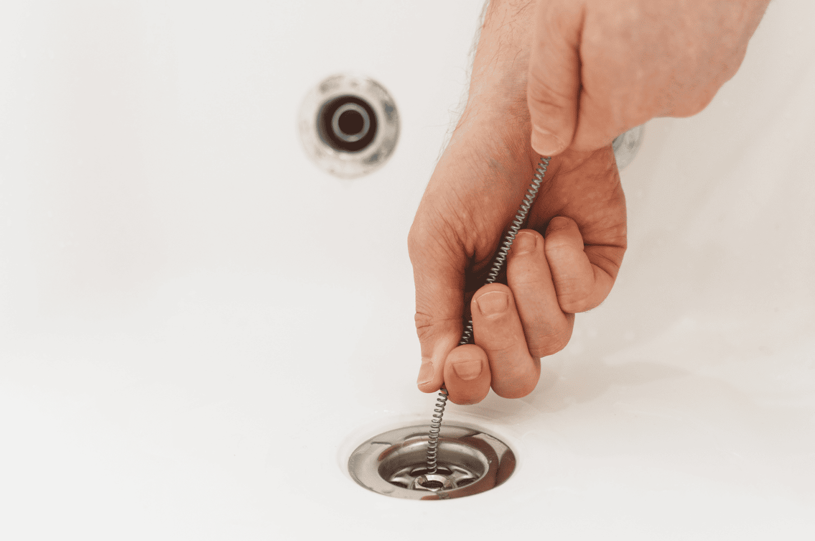 A person using a drain snake to unclog a sink drain