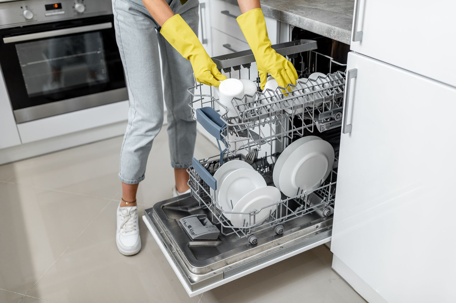 A homeowner loads a dishwasher’s top rack with white mugs