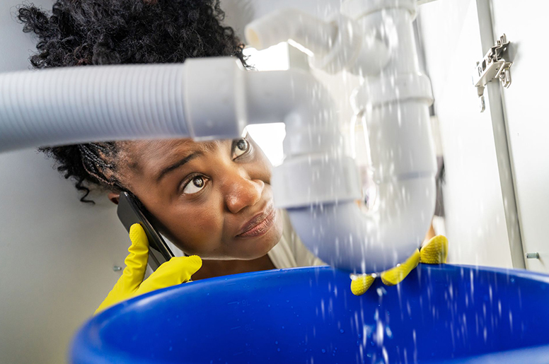 A woman making a call to an emergency plumber while looking at leaking pipes
