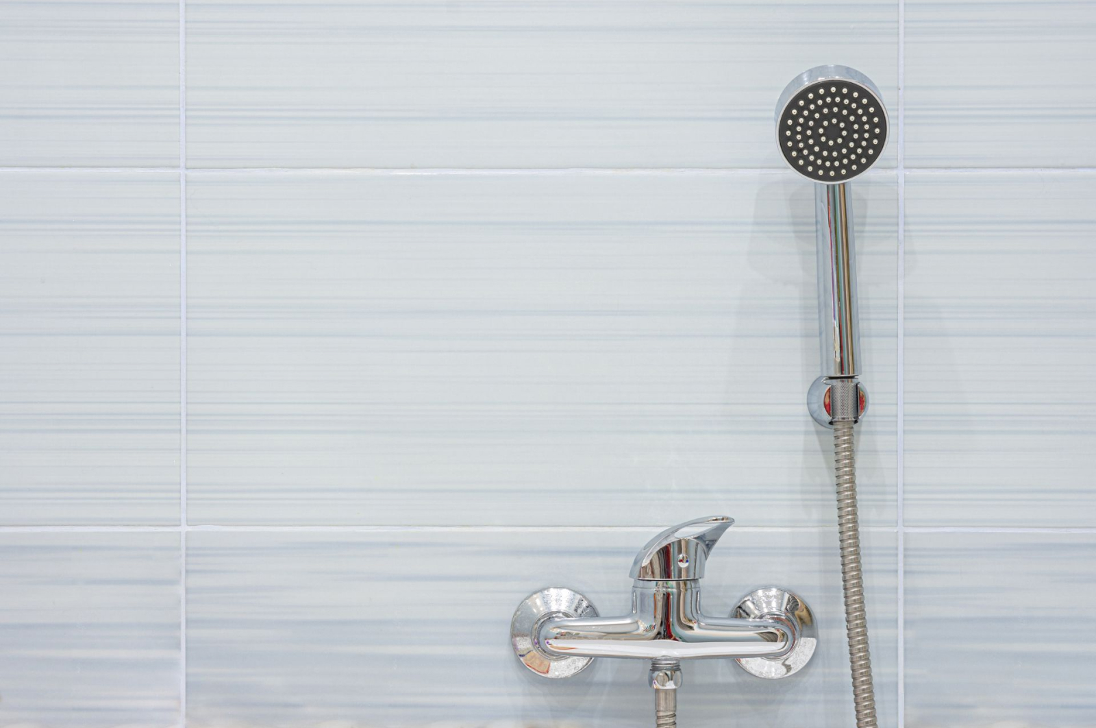 A detachable shower head mounted on a wall beside a twistable handle