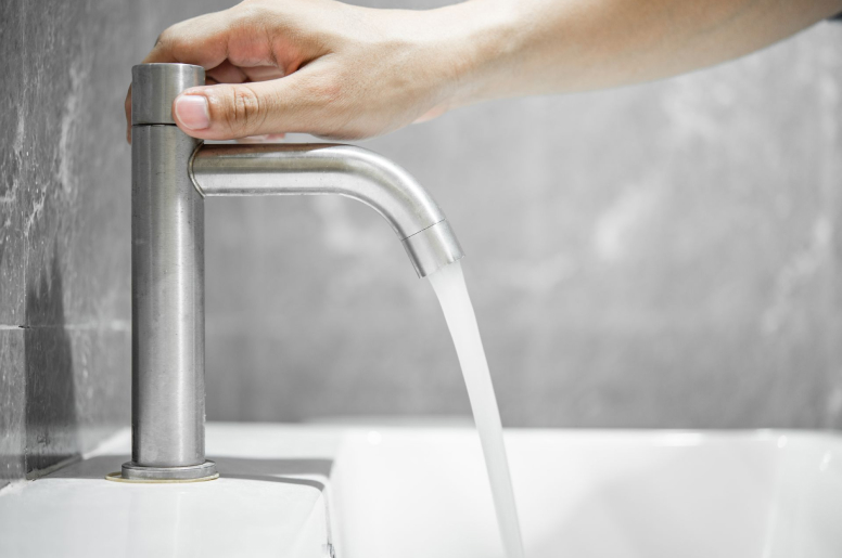 A hand twists the knob of a faucet to let water flow into the sink