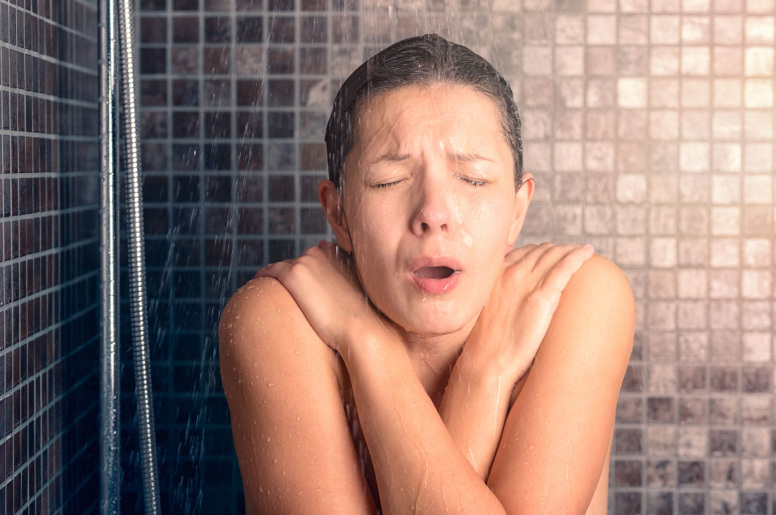 A woman shivering in the shower as cold water flows onto her