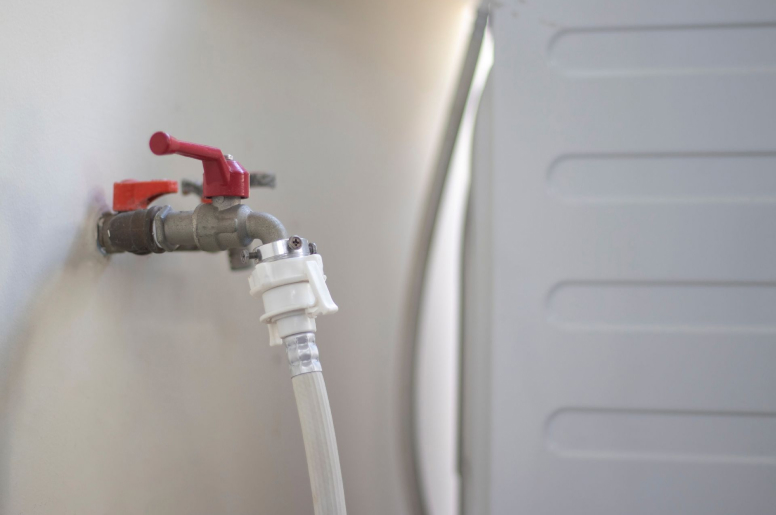 A washing machine hose connected to a washer inlet valve with a red handle on top