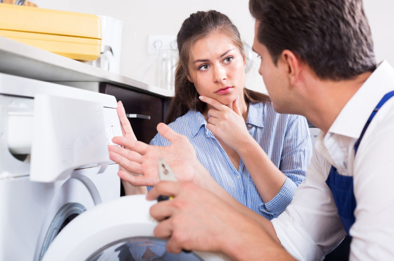 A plumber speaking to a woman while repairing her leaking washing machine