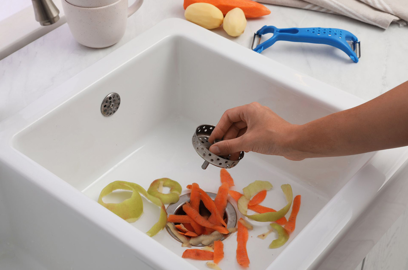 A person throwing vegetable peels into the sink garburator