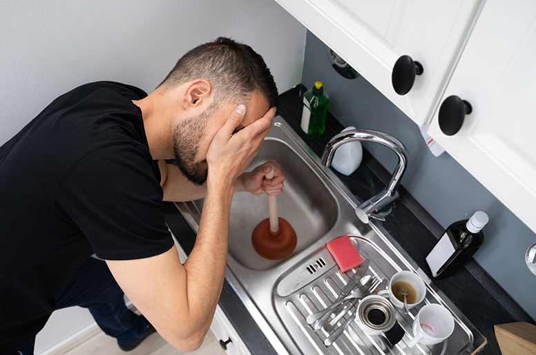 A man unclogging a kitchen sink with a plunger on the drain 